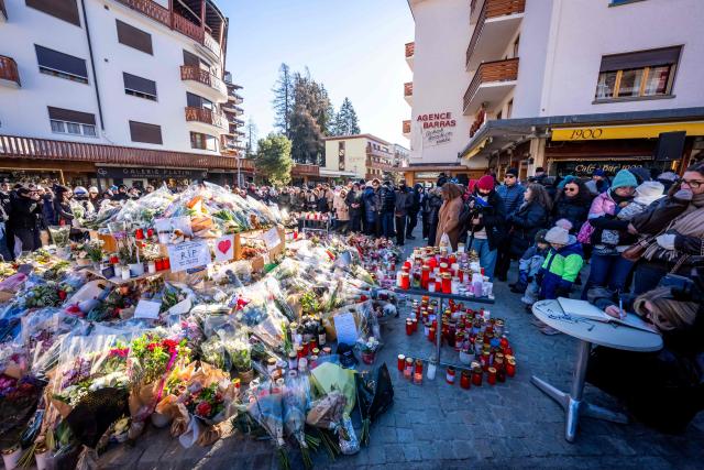 People gather around a makeshift memorial to pay their respects by laying flowers, candles and messages near the Constellation bar, on January 4, 2026, in Crans-Montana in honour of the victims of the fire that ripped through the venue in the luxury Alpine ski resort on New Year's Eve. Authorities investigating the New Year's blaze in the Swiss resort of Crans-Montana have identified 24 of the 40 people killed, including 11 minors and six foreign nationals, police said on January 4, 2026. Also 119 were injured during the fire, most of them seriously, according to the latest toll. (Photo by MAXIME SCHMID / AFP)