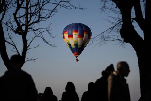 People watch hot air balloons from Mondovi Piazza, near Turin, Northwestern Italy, during the 36th International Epiphany Hot Air Balloon Rally on January 4, 2026. (Photo by MARCO BERTORELLO / AFP)