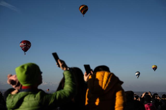 People take pictures with their phones as hot air balloons rise over Mondovi Piazza, near Turin, Northwestern Italy, during the 36th International Epiphany Hot Air Balloon Rally on January 4, 2026. (Photo by MARCO BERTORELLO / AFP)