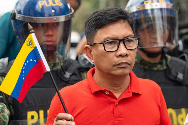 A protester holds a small Venezuelan flag as riot police stand guard during a demonstration condemning the US attack on Venezuela and the seizure of Venezuelan leader Nicolas Maduro, near the US embassy in Manila on January 5, 2026. (Photo by Ted ALJIBE / AFP)