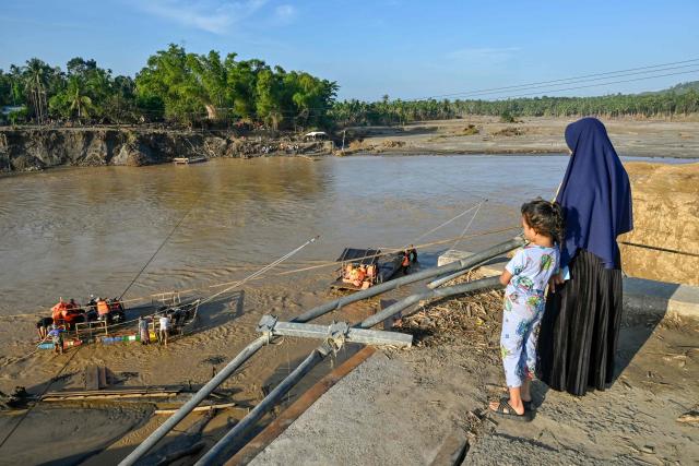 A woman and her child look at people using a rope ferry to cross the Peusangan River following flash floods that destroyed adjacent villages in Bireuen district, Indonesia's Aceh province on January 5, 2026. (Photo by CHAIDEER MAHYUDDIN / AFP/Chaideer MAHYUDDIN / AFP)