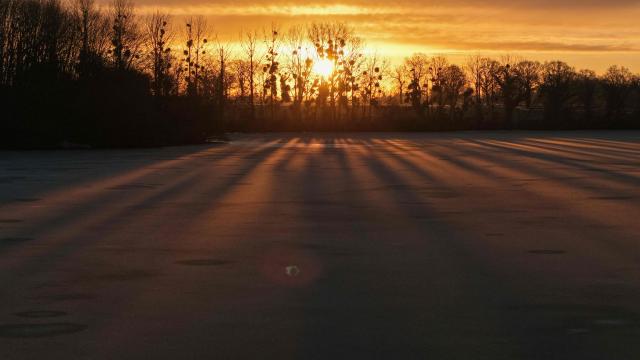 This aerial view shows a sunrise over trees and a frozen pond in Hede-Bazouges, western France on January 5, 2026. (Photo by Damien MEYER / AFP)