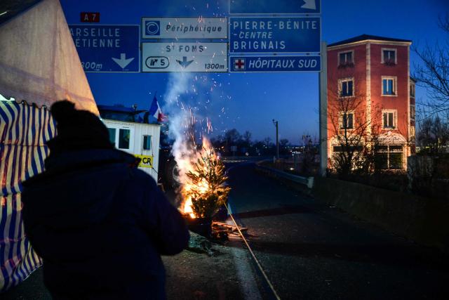 Farmers stand near a fire as they block the M7 highway in Lyon, central-eastern France, as part of a series of actions called in the region by French agricultural union Coordination Rurale (CR), on January 5, 2026. French agricultural unions take actions against a controversial free trade deal and the government's handling of a cow disease, leading to protests and roadblocks. (Photo by OLIVIER CHASSIGNOLE / AFP)