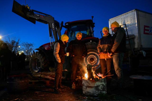 Farmers warm themselves by a fire as they block the M7 highway in Lyon, central-eastern France, as part of a series of actions called in the region by French agricultural union Coordination Rurale (CR), on January 5, 2026. French agricultural unions take actions against a controversial free trade deal and the government's handling of a cow disease, leading to protests and roadblocks. (Photo by OLIVIER CHASSIGNOLE / AFP)