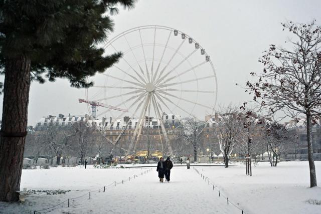A couple walks near the ferris wheel at the Jardin des Tuileries covered in snow in Paris on January 5, 2026. (Photo by Christophe DELATTRE / AFP)