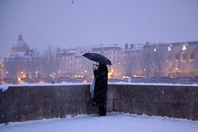 A pedestrian holds an umbrella at the Pont du Carrousel covered in snow in Paris on January 5, 2026. (Photo by Christophe DELATTRE / AFP)