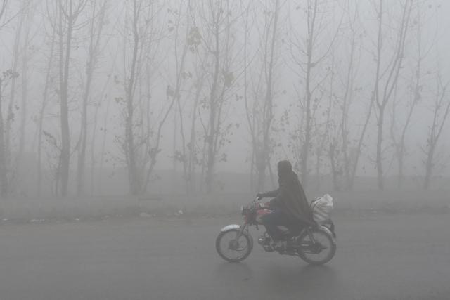 A motorist rides his bike amid dense fog on a winter morning in Peshawar on January 6, 2026. (Photo by Abdul MAJEED / AFP)