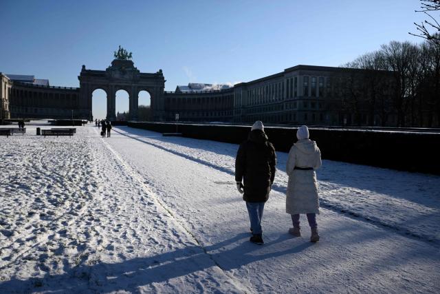 Pedestrians walk in the snow-covered Parc du Cinquantenaire in Brussels, on January 6, 2026. (Photo by Nicolas TUCAT / AFP)