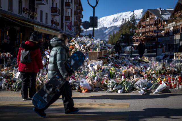 A young snowboarder walks past a makeshift memorial with laying flowers, candles and messages near the Constellation bar in Crans-Montana on January 6, 2026, in honour of the victims of the fire that ripped through the venue in the luxury Alpine ski resort on New Year's Eve. (Photo by Fabrice COFFRINI / AFP)
