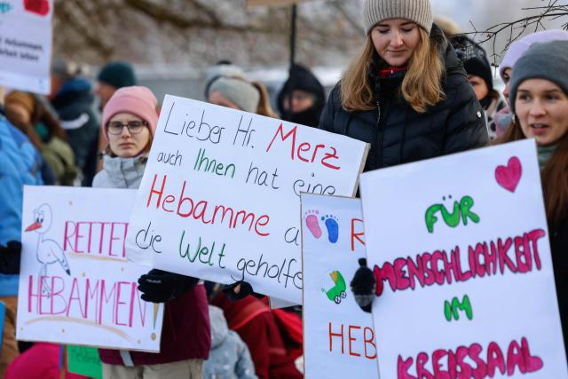 Midwifes and family members protest with placards against the "Hebammenhilfe-Vertrag" (Midwifery Care Agreement) on the sidelines of the CSU party faction retreat at Seeon Abbey in Seeon, southern Germany, on January 6, 2026. A controversial new midwifery care agreement entered into force on November 1, 2025 and sparks fears that many midwives could stop exercising. (Photo by Michaela STACHE / AFP)
