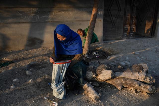 An Afghan woman knits a garment sleeve along a roadside on the outskirts of Mazar-i-Sharif on January 6, 2026. (Photo by Atif ARYAN / AFP)