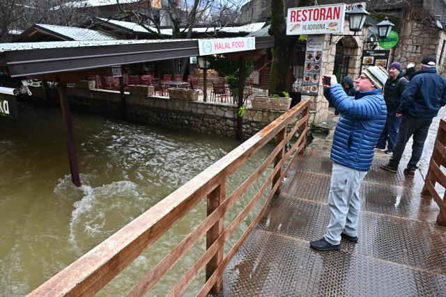 A man takes photographs of flooded restaurants on the bank, near the spring of river Buna, following heavy rain in southern-Bosnian town of Blagaj on January 6, 2026. Snow and heavy rains sparked power failures and flooding in parts of the Balkans, authorities said on January 6, 2026, with one woman dead in a weather-related accident in Bosnia. (Photo by ELVIS BARUKCIC / AFP)