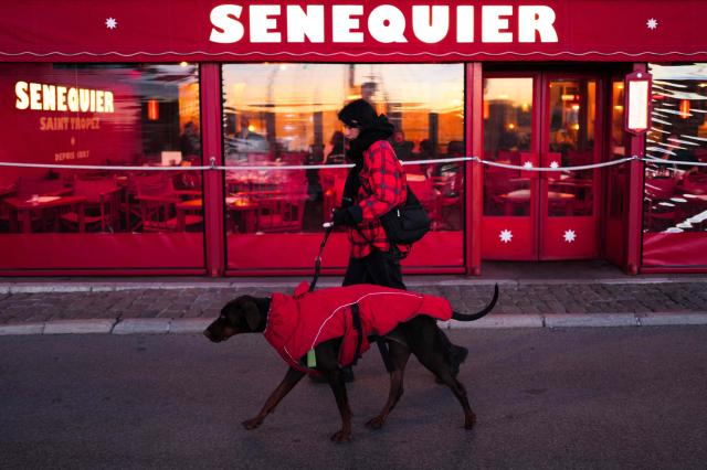 A woman walks with her dog past the Senequier restaurant in Saint-Tropez, southeastern France on January 6, 2026. (Photo by Valery HACHE / AFP)