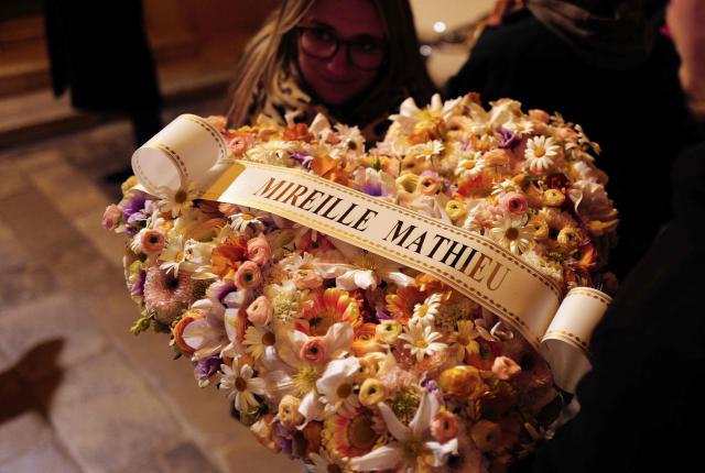 A florist holds a bunch of flowers reading "Mireille Mathieu" at Notre-Dame de l'Assomption church on the eve of the funeral ceremony of late French actress Brigitte Bardot in Saint-Tropez, southeastern France on January 6, 2026. (Photo by Valery HACHE / AFP)