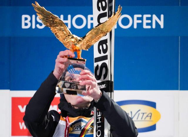 Overall winner Slovenia's Domen Prevc celebrates with the trophy on the podium after the Men's Individual Large Hill HS142 event of the FIS Ski Jumping World Cup, the fourth and last leg of the Four Hills Tournament, in Bischofshofen, Austria on January 6, 2026. (Photo by GEORG HOCHMUTH / APA / AFP) / Austria OUT