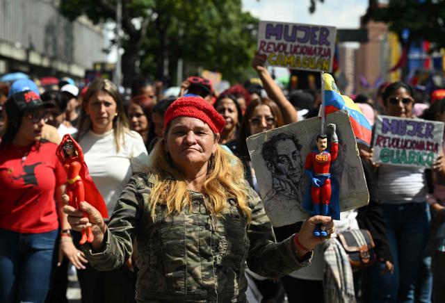 A woman holds toys of the caped superhero named "Super-Bigote" (Super-Mustache) and "Cilita," during a rally in support of ousted Venezuela's President Nicolas Maduro and his wife Cilia Flores in Caracas on January 6, 2026. US forces killed 55 Venezuelan and Cuban military personnel during their stunning raid to capture Nicolas Maduro, tolls published by Caracas and Havana showed on January 6. (Photo by RONALDO SCHEMIDT / AFP)
