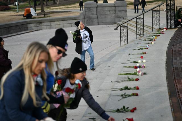 People place flowers at the US Capitol as Michelle “Micki” Witthoeft (R), mother of killed January 6 rioter Ashli Babbitt, looks on as people march to the Capitol in a rally promoted by right-wing activists on the fifth anniversary of the January 6 riots in Washington, DC, on January 6, 2026. Washington on Tuesday marks five years since a mob overran the US Capitol, with rioters pardoned by Donald Trump retracing their steps even as Democrats revive hearings to hold the president accountable. The anniversary highlights a nation divided between irreconcilable accounts of an attack that reshaped American politics -- one supported by official findings of a violent bid to overturn an election, the other portraying it as a protest unjustly criminalized. (Photo by Brendan SMIALOWSKI / AFP)