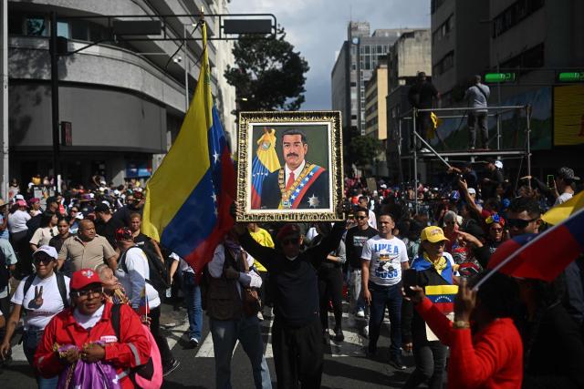 A man holds a picture of ousted Venezuelan President Nicolas Maduro during a rally in support of Maduro and his wife, Cilia Flores, in Caracas on January 6, 2026. US forces killed 55 Venezuelan and Cuban military personnel during their stunning raid to capture Nicolas Maduro, tolls published by Caracas and Havana showed on January 6. (Photo by Federico PARRA / AFP)