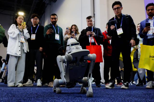 Attendees watch a Kami Vision ZL robot as it walks around at the annual Consumer Electronics Show (CES) in Las Vegas, Nevada, on January 6, 2026. Kami Vision specializes in smart security and senior safety solutions. (Photo by Caroline Brehman / AFP)