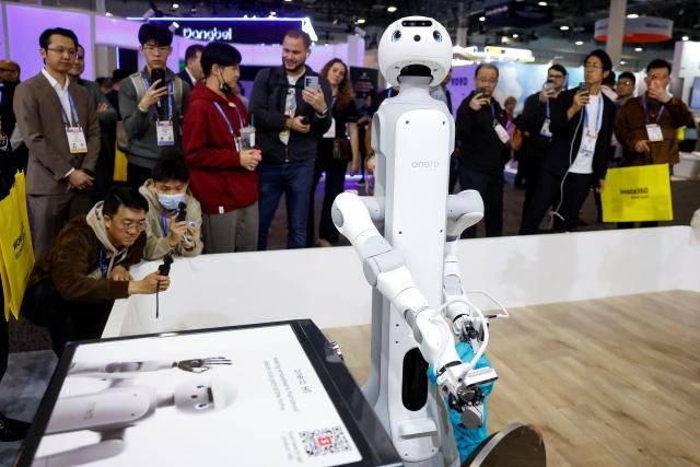 SwitchBot’s Onero H1 robot, which uses cameras, articulated arms and an on-device AI model to perform household tasks, puts an item of clothing into a washing machine at the annual Consumer Electronics Show (CES) in Las Vegas, Nevada, on January 6, 2026. (Photo by Caroline Brehman / AFP)