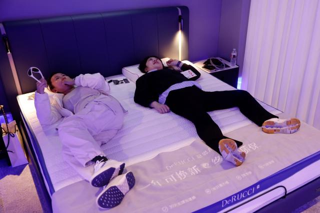Attendees try out the DeRUCCI AI mattress that uses sensors and AI to monitor sleep biometrics and automatically adjust mechanisms to enhance the users' sleep at the annual Consumer Electronics Show (CES) in Las Vegas, Nevada, on January 6, 2026. (Photo by Caroline Brehman / AFP)