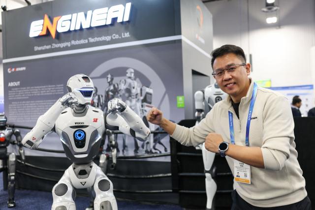 Evan Yao of EngineAI poses with the EngineAI T800 humanoid robot during the annual Consumer Electronics Show (CES) in Las Vegas, Nevada on January 6, 2026. (Photo by Patrick T. Fallon / AFP)