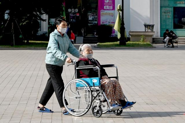 A woman pushes an elderly person in a wheelchair in Hanoi on January 7, 2026. (Photo by Nhac NGUYEN / AFP)
