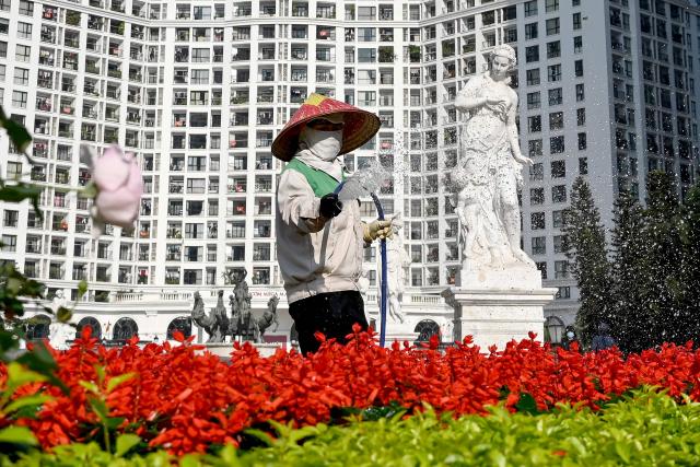 A worker waters flowers in front of a high-rise apartment building in Hanoi on January 7, 2026. (Photo by Nhac NGUYEN / AFP)