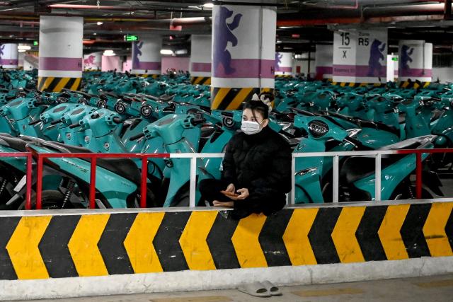 A woman sits next to electric motorcycles in a parking lot in Hanoi on January 7, 2026. (Photo by Nhac NGUYEN / AFP)