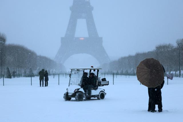 A couple holds an umbrella in front of the Eiffel Tower during a snowfall in Paris on January 7, 2026. Snow and ice are affecting northern and western France, a phenomenon of “rare magnitude in the current climate” according to Meteo-France, which is expected to cause significant restrictions on roads and air transport. (Photo by Ludovic MARIN / AFP)