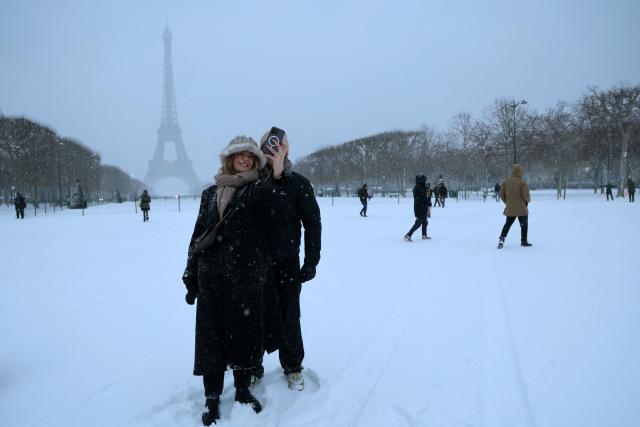 People take a selfie in front of the Eiffel Tower during a snowfall in Paris on January 7, 2026. Snow and ice are affecting northern and western France, a phenomenon of “rare magnitude in the current climate” according to Meteo-France, which is expected to cause significant restrictions on roads and air transport. (Photo by Ludovic MARIN / AFP)