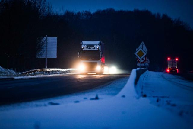 Cars and truck drive along a road as snow falls in Lisieux, northwestern France, on January 7, 2026. Snow and ice are affecting northern and western France, a phenomenon of “rare magnitude in the current climate” according to Meteo-France, which is expected to cause significant restrictions on roads and air transport. (Photo by Lou BENOIST / AFP)