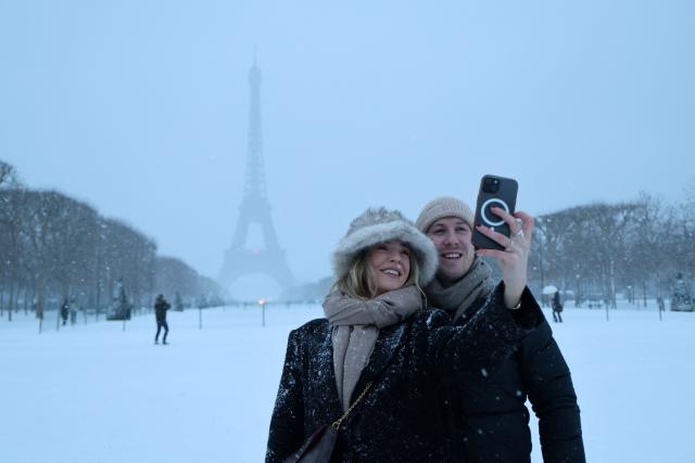 A couple takes a selfie in front of the Eiffel Tower during a snowfall in Paris on January 7, 2026. Snow and ice are affecting northern and western France, a phenomenon of “rare magnitude in the current climate” according to Meteo-France, which is expected to cause significant restrictions on roads and air transport. (Photo by Ludovic MARIN / AFP)