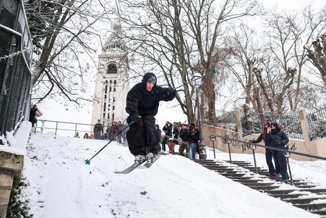 A skier jumps down a snow-covered slope next to spectating pedestrians at Montmartre following snowfalls in Paris, on January 7, 2026. All buses in Paris and the surrounding region gradually stopped running at around 7am due to renewed snowfall in the area and returned to their depots, according to announcements by Ile-de-France Mobilitйs (IDFM) and RATP. Snow and ice are affecting northern and western France, a phenomenon of “rare magnitude in the current climate” according to Meteo-France, which is expected to cause significant restrictions on roads and air transport. (Photo by Anne-Christine POUJOULAT / AFP)