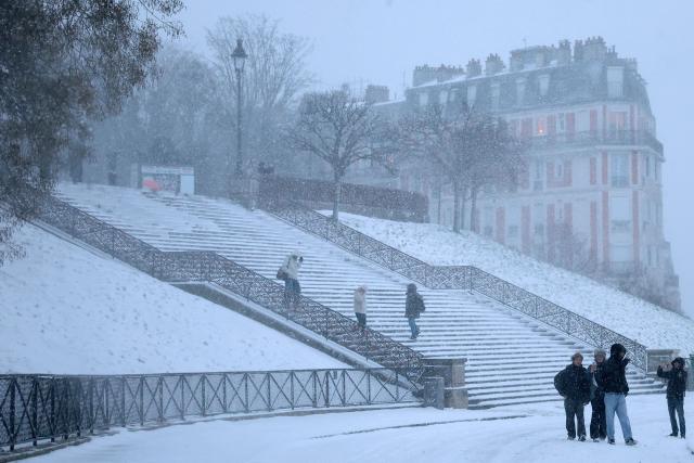 People gather at the bottom of the stairs in Montmartre, during heavy snow falls, in Paris, on January 7, 2026. All buses in Paris and the surrounding region gradually stopped running at around 7am due to renewed snowfall in the area and returned to their depots, according to announcements by Ile-de-France Mobilitйs (IDFM) and RATP. Snow and ice are affecting northern and western France, a phenomenon of “rare magnitude in the current climate” according to Meteo-France, which is expected to cause significant restrictions on roads and air transport. (Photo by Anne-Christine POUJOULAT / AFP)
