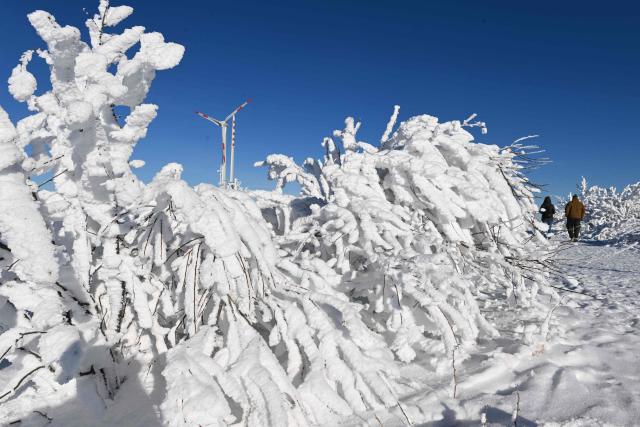 People walk through the landscape covered in frost and snow on the Hornisgrinde mountain near Seebach in the Northern Black Forest, southern Germany, during a cold and sunny day on January 7, 2026. (Photo by THOMAS KIENZLE / AFP)
