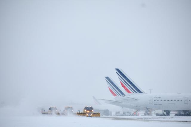 Air France airplanes are seen on the tarmac as snowplows clear the runways after heavy snowfalls, which caused flight cancellations at Orly Airport, south of Paris on January 7, 2026. Around 100 flights were cancelled at Paris's Charles de Gaulle airport because of snowfall and fierce cold, and a further 40 were cancelled at Orly airport, France's transport minister said. (Photo by Kiran RIDLEY / AFP)
