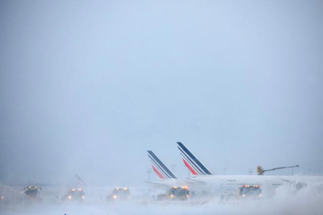 Air France airplanes are seen on the tarmac as snowplows clear the runways after heavy snowfalls, which caused flight cancellations at Orly Airport, south of Paris on January 7, 2026. Around 100 flights were cancelled at Paris's Charles de Gaulle airport because of snowfall and fierce cold, and a further 40 were cancelled at Orly airport, France's transport minister said. (Photo by Kiran RIDLEY / AFP)