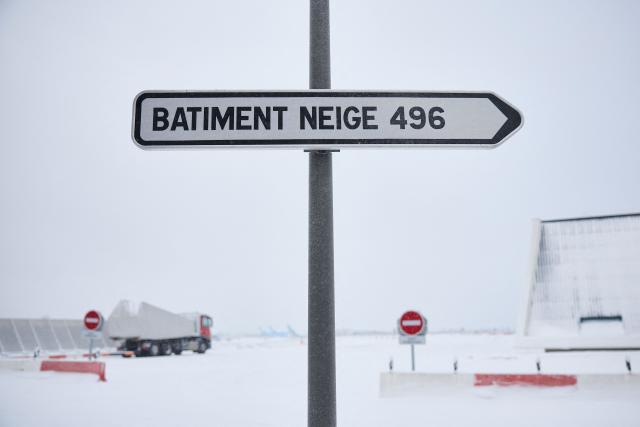 This photograph shows a sign indicating the way to the "snow building" after heavy snowfalls which caused flight cancellations at Orly Airport, south of Paris on January 7, 2026. Around 100 flights were cancelled at Paris's Charles de Gaulle airport because of snowfall and fierce cold, and a further 40 were cancelled at Orly airport, France's transport minister said. (Photo by Kiran RIDLEY / AFP)