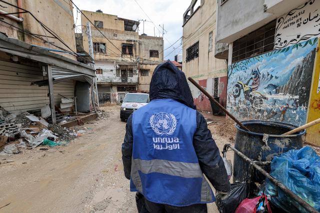 (FILES) A man collects trash while wearing a jacket bearing the logo of the United Nations Relief and Works Agency for Palestine Refugees in the Near East (UNRWA), along a street in the city of Jenin in the occupied West Bank on January 30, 2024. The UN's agency for Palestinian refugees said on January 7, 2026 that a "dire" financial crisis had this week forced it to fire hundreds of Gazan staff, who had left the territory. (Photo by Jaafar ASHTIYEH / AFP)