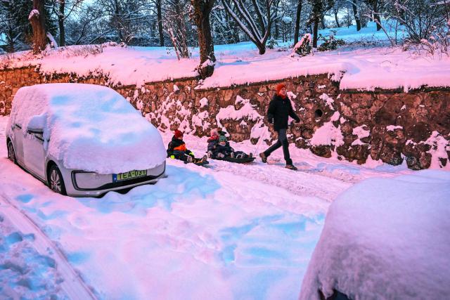 A young father pulls his children's sled on the snowy road in Budapest, Hungary as the first snow of the year 2026 fell on the Hungarian capital, on January 7, 2026. (Photo by Attila KISBENEDEK / AFP)