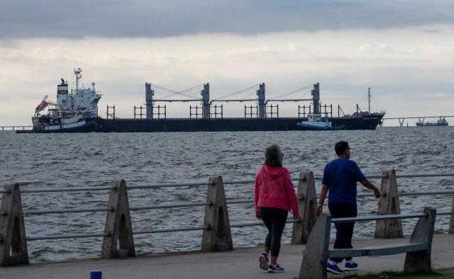 People walk through a walkway as crude oil tankers are seen anchored on Lake Maracaibo in the background on January 7, 2026. US Energy Secretary Chris Wright said in January 7, Washington will control sales of Venezuelan oil "indefinitely," a day after President Donald Trump announced Venezuela's interim leaders had agreed to US-managed marketing of 30-50 million barrels of crude. (Photo by Maryorin Mendez / AFP)
