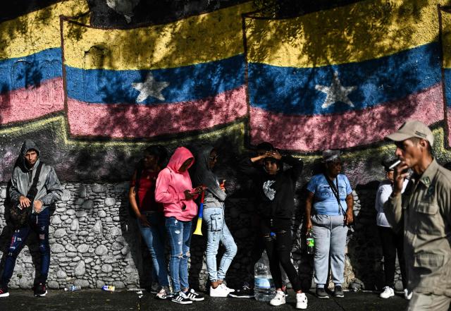 People stand in front of a mural with a Venezuelan flag in Caracas on January 7, 2026. US President Donald Trump's administration said on January 7, it intends to dictate the decisions of Venezuela's interim leaders and control the country's oil sales "indefinitely" after toppling Nicolas Maduro. (Photo by Ronaldo SCHEMIDT / AFP)