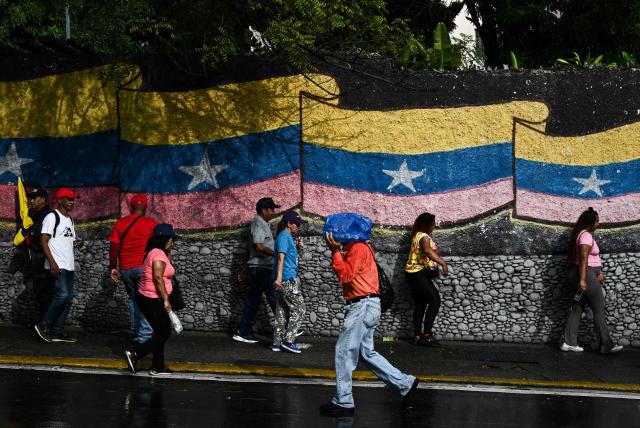 People stand in front of a mural with a Venezuelan flag in Caracas on January 7, 2026. US President Donald Trump's administration said on January 7, it intends to dictate the decisions of Venezuela's interim leaders and control the country's oil sales "indefinitely" after toppling Nicolas Maduro. (Photo by Ronaldo SCHEMIDT / AFP)