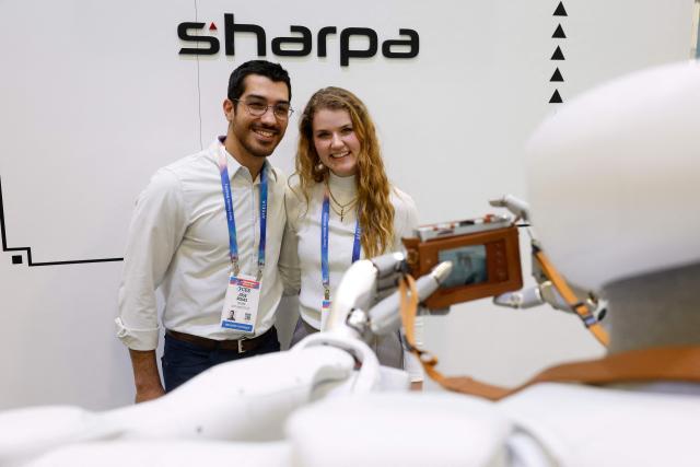 People pose as the Sharpa robot takes a photo with a Fujifilm instax camera during the annual Consumer Electronics Show (CES) in Las Vegas, Nevada, on January 7, 2026. (Photo by Caroline Brehman / AFP)
