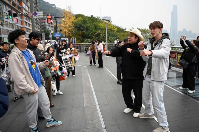 The photo taken on December 15, 2025 shows Donald Trump's impersonator Ryan Chen dancing to song "YMCA" with fans along a street in southwestern China's Chongqing municipality. Outstretching his hands in a signature Donald Trump pose, impersonator Ryan Chen mimics the US president's voice and gestures with such accuracy he has become a social media phenomenon with his funny videos. (Photo by Jade GAO / AFP) / TO GO WITH: China-US-social-comedy-Trump, PROFILE by Ludovic EHRET