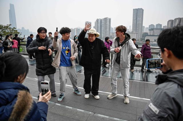 The photo taken on December 15, 2025 shows Donald Trump's impersonator Ryan Chen dancing to song "YMCA" with fans along a street in southwestern China's Chongqing municipality. Outstretching his hands in a signature Donald Trump pose, impersonator Ryan Chen mimics the US president's voice and gestures with such accuracy he has become a social media phenomenon with his funny videos. (Photo by Jade GAO / AFP) / TO GO WITH: China-US-social-comedy-Trump, PROFILE by Ludovic EHRET