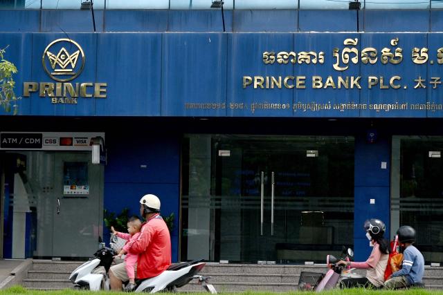 (FILES) Motorists ride past a branch of the Prince Bank in Phnom Penh on October 15, 2025. A Cambodian bank founded by accused scam boss Chen Zhi, who has been indicted by the United States and extradited to China, was ordered liquidated on January 8, 2026, Cambodia's central bank said. (Photo by TANG CHHIN Sothy / AFP)