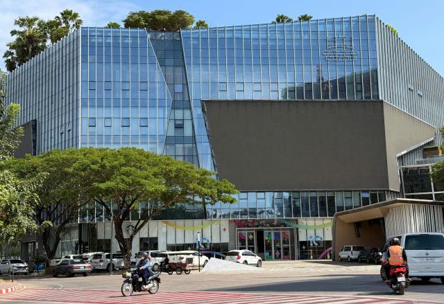 Motorists ride past the Prince Group Headquarters in Phnom Penh on January 8, 2026. A Cambodian bank founded by accused scam boss Chen Zhi, who has been indicted by the United States and extradited to China, was ordered liquidated on January 8, 2026, Cambodia's central bank said. (Photo by Suy SE / AFP)