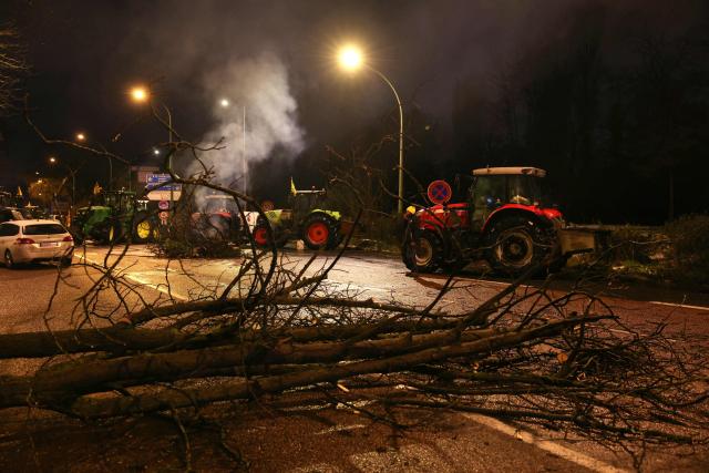 Branches are placed across a road as people gather next to tractors during a demonstration of French agricultural union Coordination Rurale (CR) as part of a nationwide day of protests and actions called by several farmers unions to push the French government to block the Mercosur trade deal and protest against its handling of the nodular dermatitis (CND) epidemic, near the Porte d'Auteuil metro station in Paris on January 8, 2026. (Photo by Thomas SAMSON / AFP)
